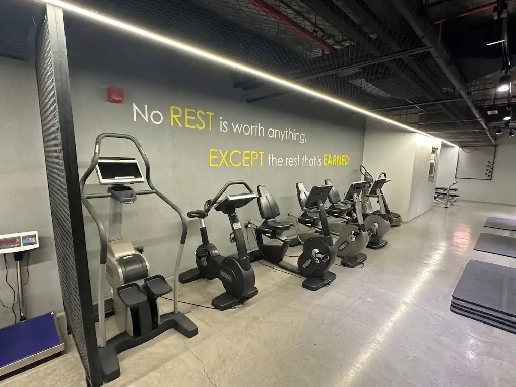 Cardio machines beneath the Fitness Avenue wall mural reading No Rest is worth anything, except the rest that is earned